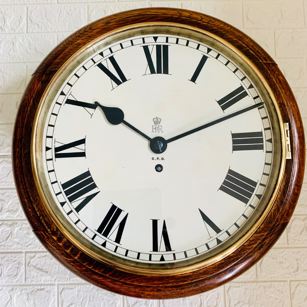 A circular wooden wall clock with a white dial, Roman numerals, black hands, and official G.P.O. markings set within a brass bezel. View VII