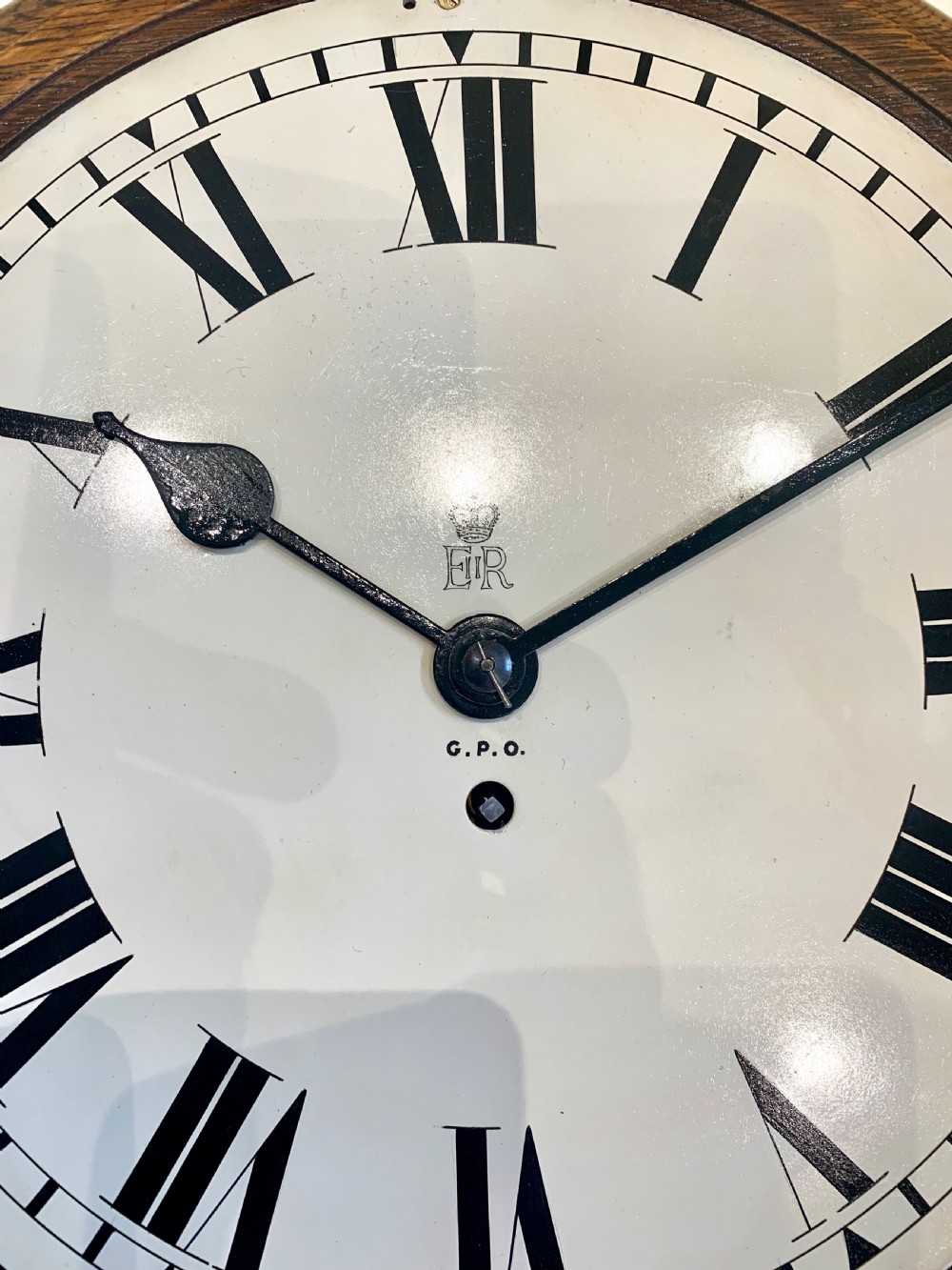A circular wooden wall clock with a white dial, Roman numerals, black hands, and official G.P.O. markings set within a brass bezel. View VIII