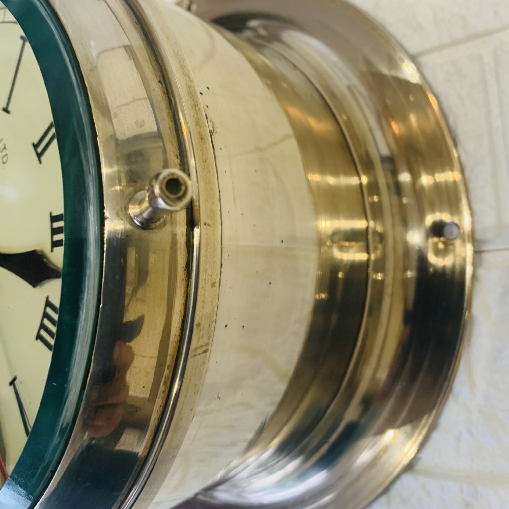A circular brass maritime bulkhead wall clock with a cream dial face, Roman numerals, spade hands, and Henry Browne and Son Sestrel branding. View II