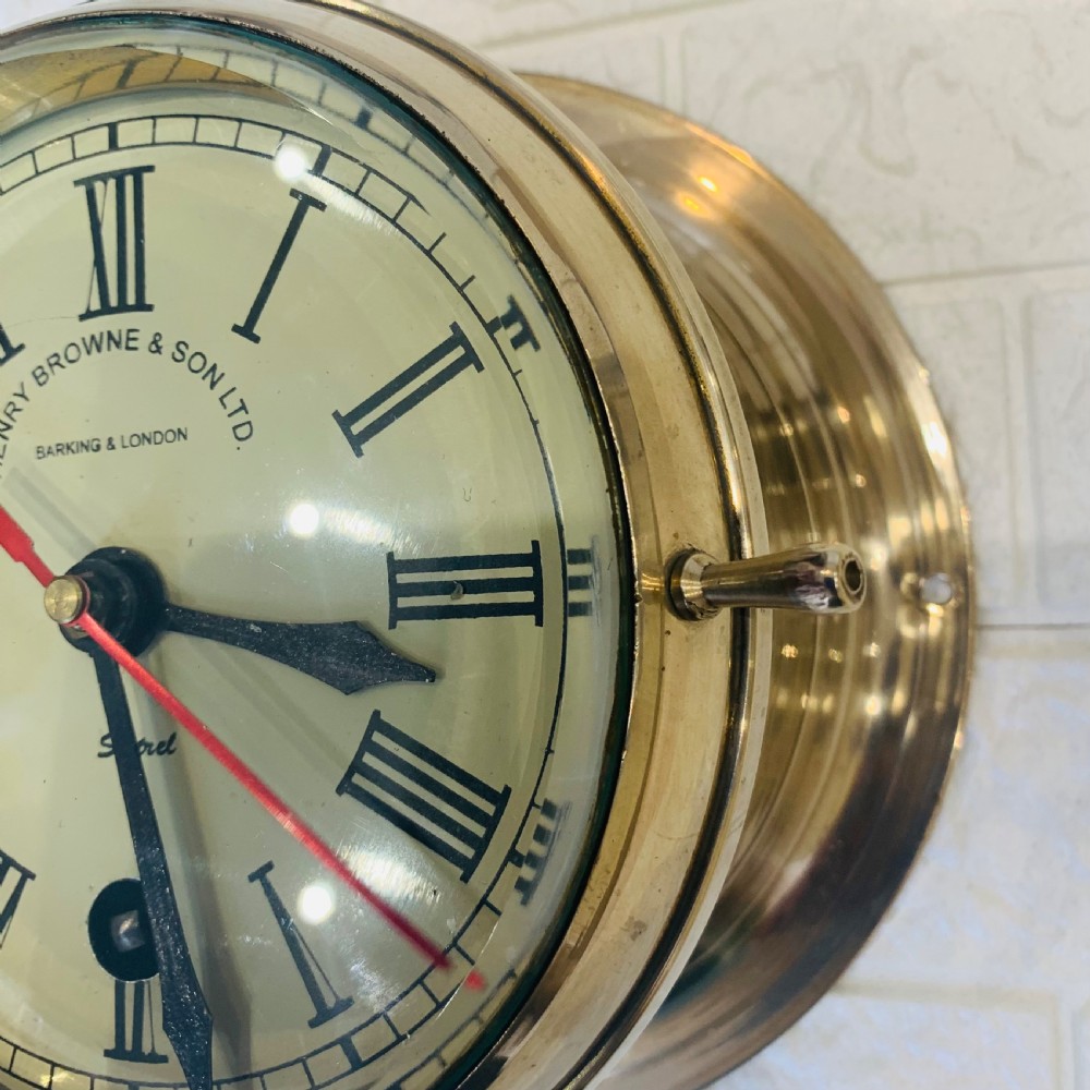 A circular brass maritime bulkhead wall clock with a cream dial face, Roman numerals, spade hands, and Henry Browne and Son Sestrel branding. View IV