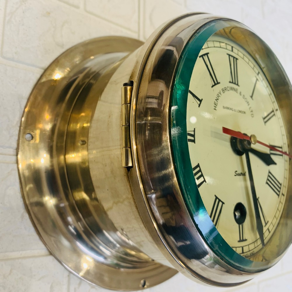 A circular brass maritime bulkhead wall clock with a cream dial face, Roman numerals, spade hands, and Henry Browne and Son Sestrel branding. View V