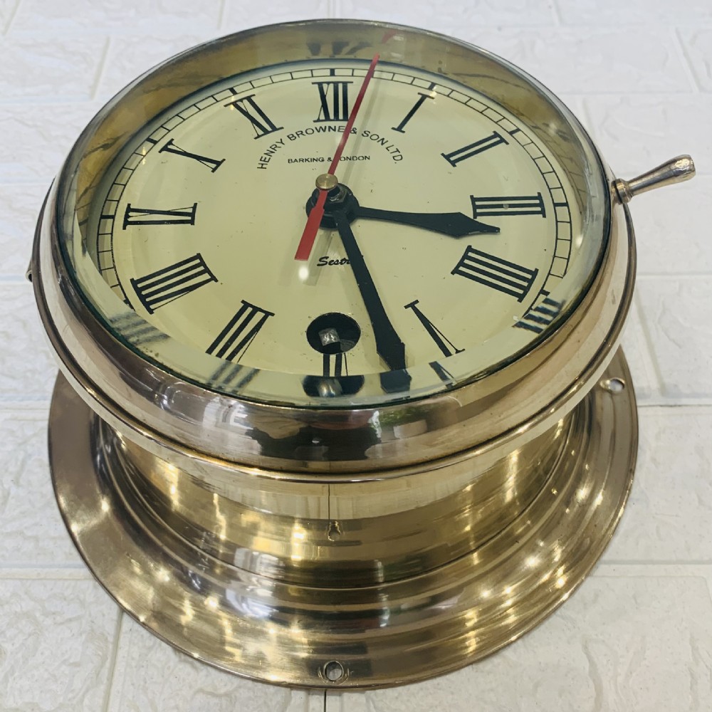 A circular brass maritime bulkhead wall clock with a cream dial face, Roman numerals, spade hands, and Henry Browne and Son Sestrel branding. View VII