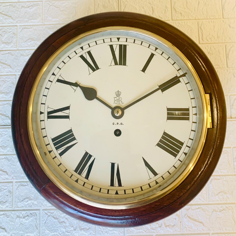 A circular dark wood wall clock featuring a white dial with black Roman numerals, brass bezel, and GPO EIIR markings.