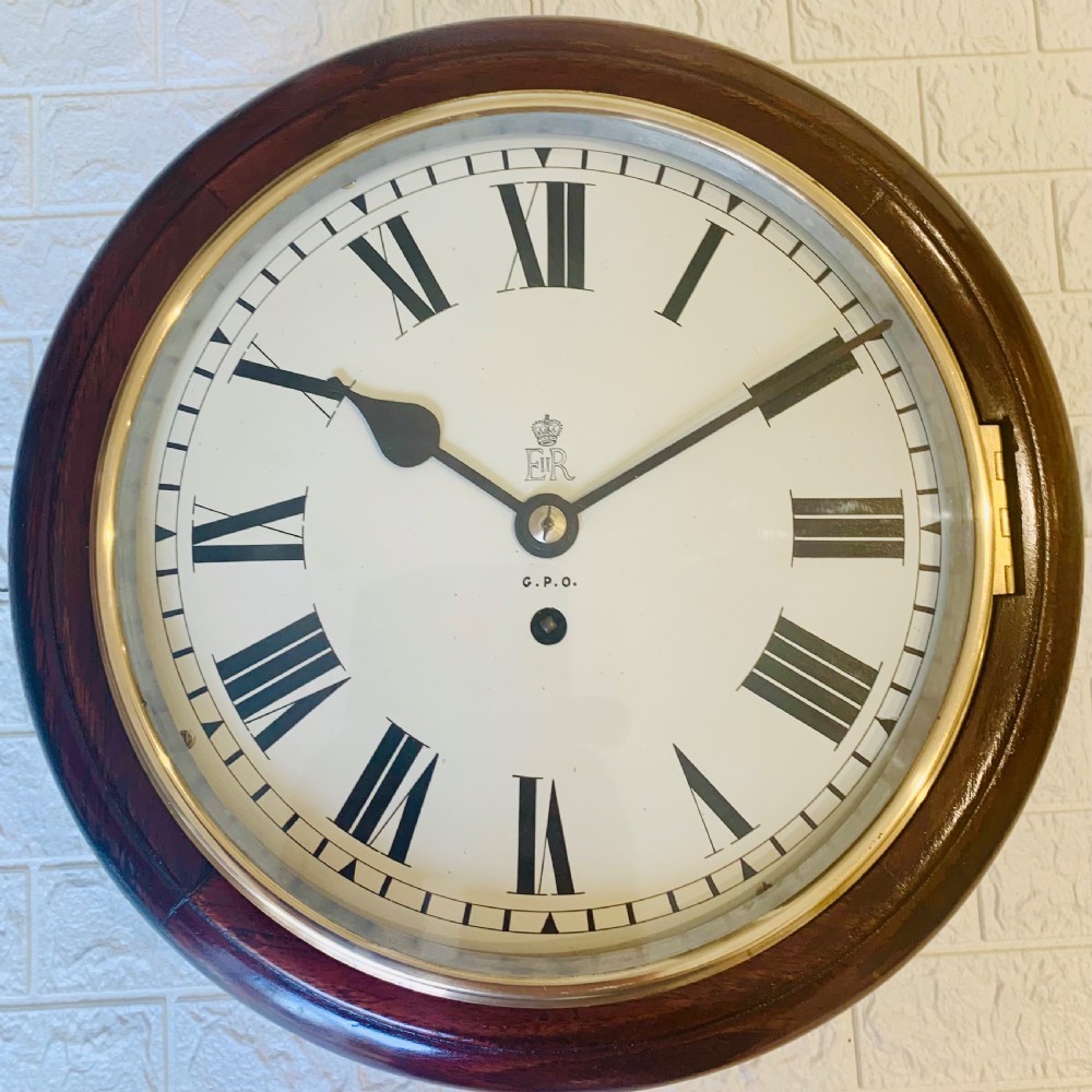 A circular dark wood wall clock featuring a white dial with black Roman numerals, brass bezel, and GPO EIIR markings. View II