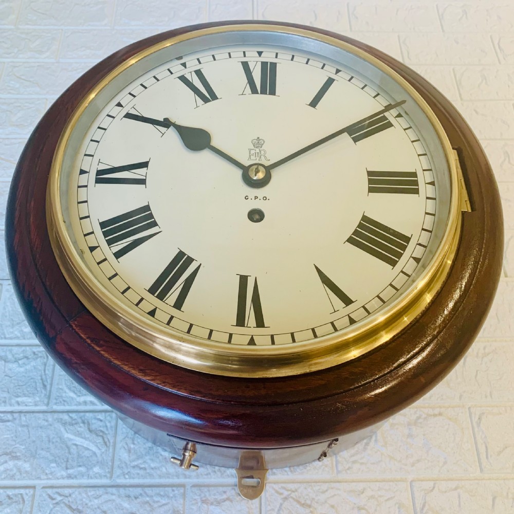 A circular dark wood wall clock featuring a white dial with black Roman numerals, brass bezel, and GPO EIIR markings. View III