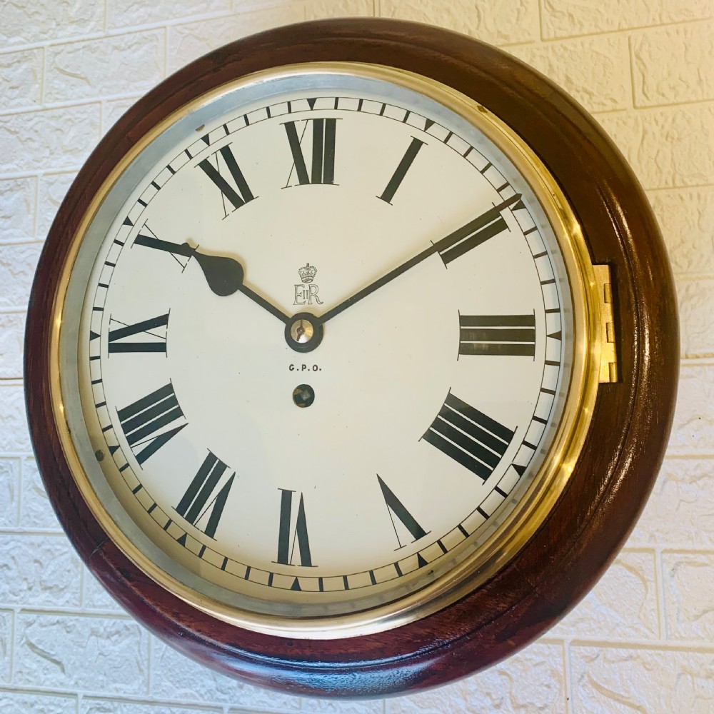 A circular dark wood wall clock featuring a white dial with black Roman numerals, brass bezel, and GPO EIIR markings. View IV