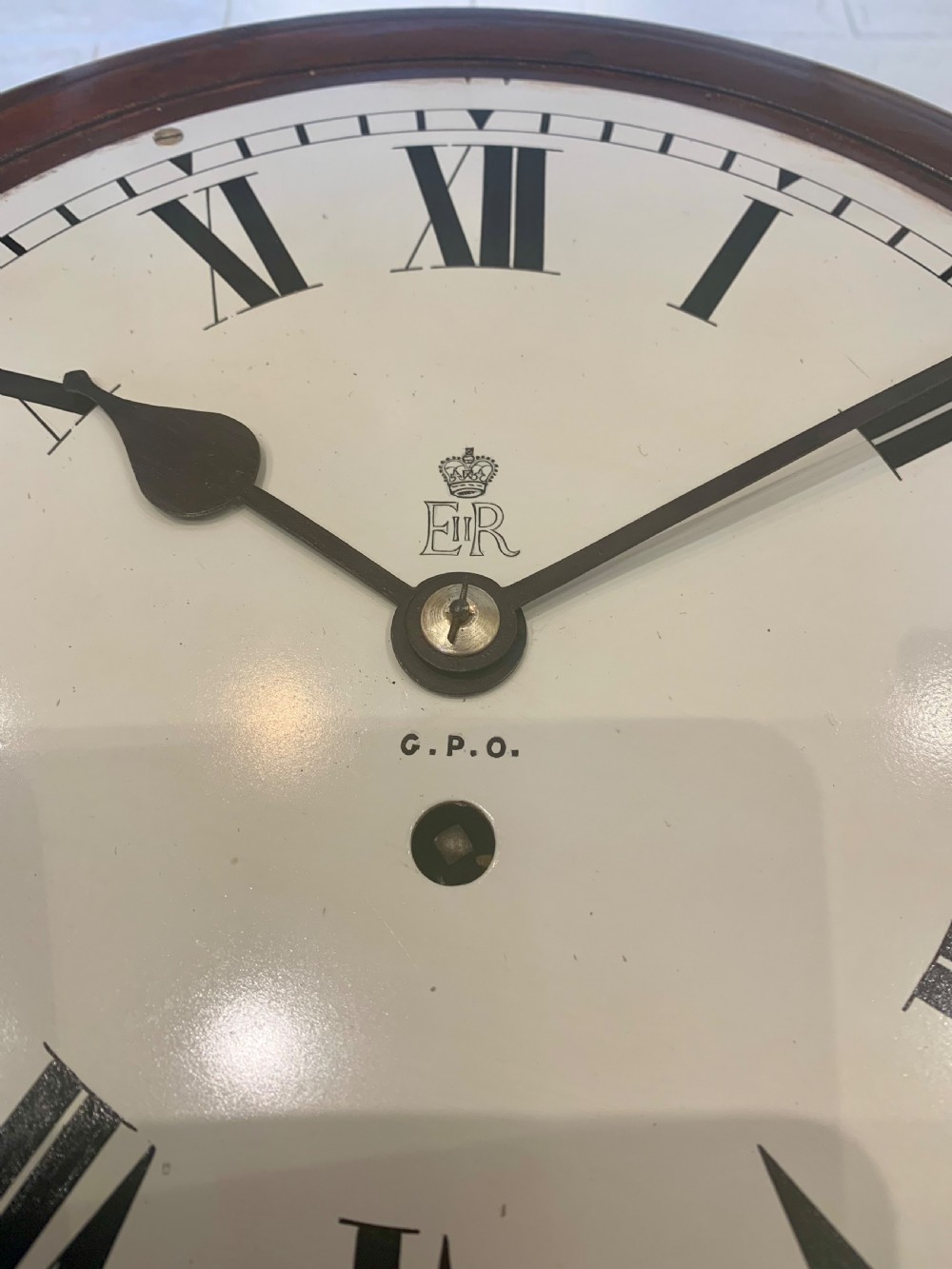 A circular dark wood wall clock featuring a white dial with black Roman numerals, brass bezel, and GPO EIIR markings. View V