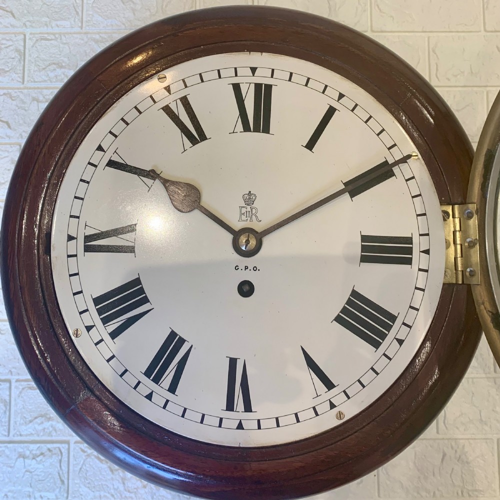 A circular dark wood wall clock featuring a white dial with black Roman numerals, brass bezel, and GPO EIIR markings. View VI