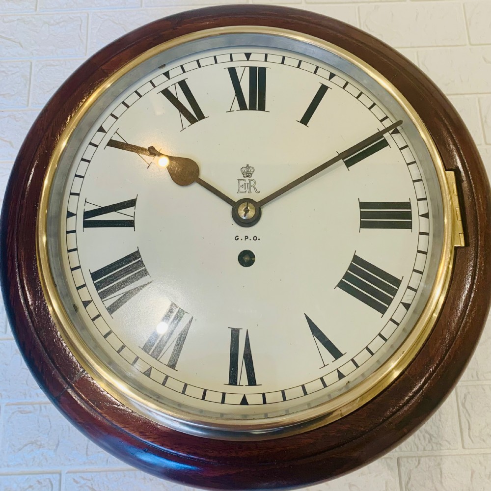 A circular dark wood wall clock featuring a white dial with black Roman numerals, brass bezel, and GPO EIIR markings. View VII