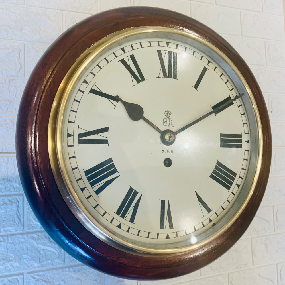 A circular dark wood wall clock featuring a white dial with black Roman numerals, brass bezel, and GPO EIIR markings. View VIII