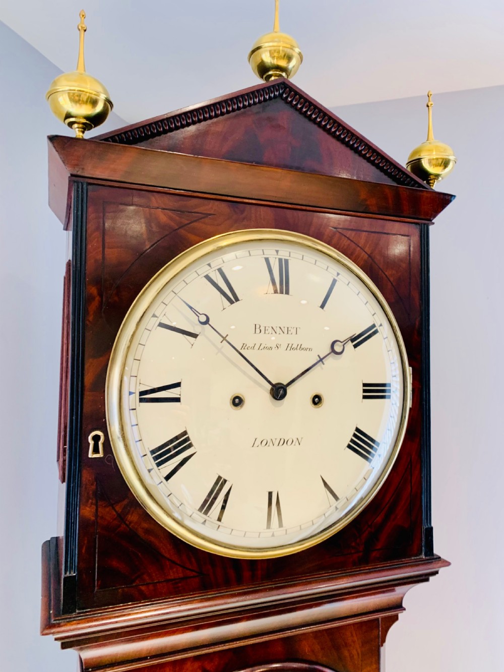 A Regency flame mahogany longcase clock featuring a circular dial signed Bennet London, topped with a pediment and three brass ball finials. View III
