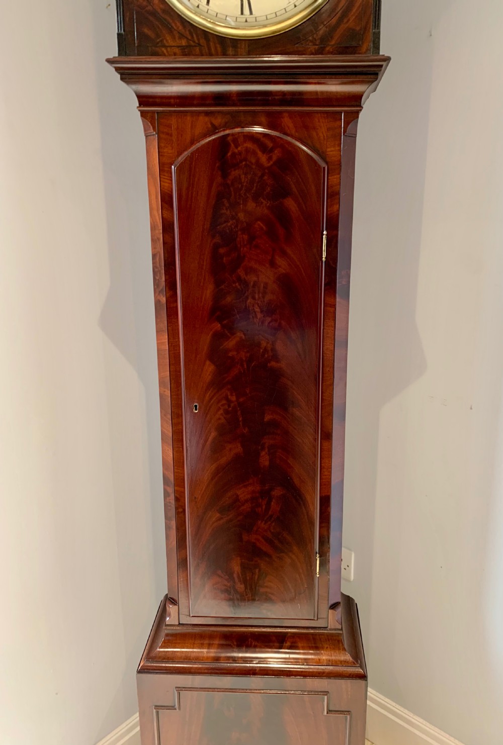 A Regency flame mahogany longcase clock featuring a circular dial signed Bennet London, topped with a pediment and three brass ball finials. View X