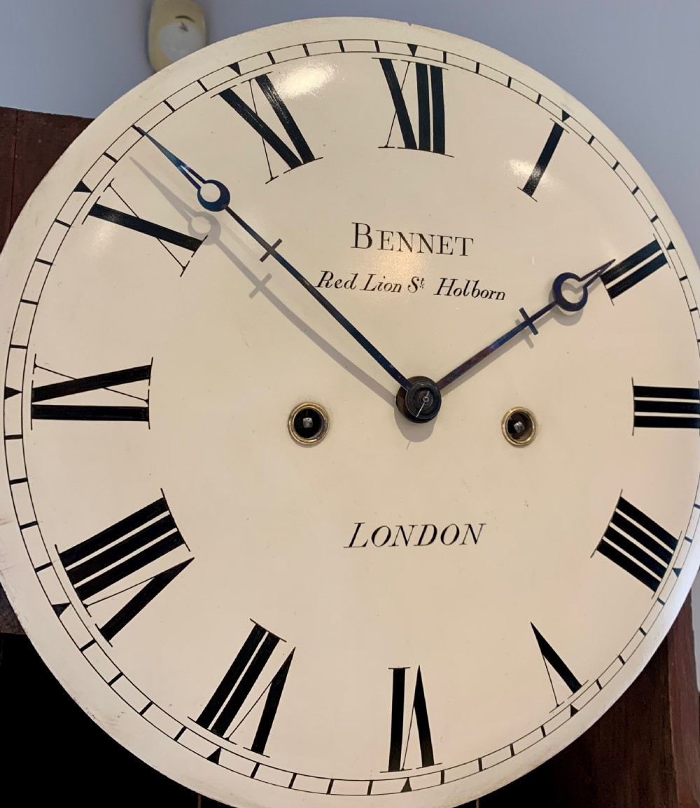 A Regency flame mahogany longcase clock featuring a circular dial signed Bennet London, topped with a pediment and three brass ball finials. View XVI