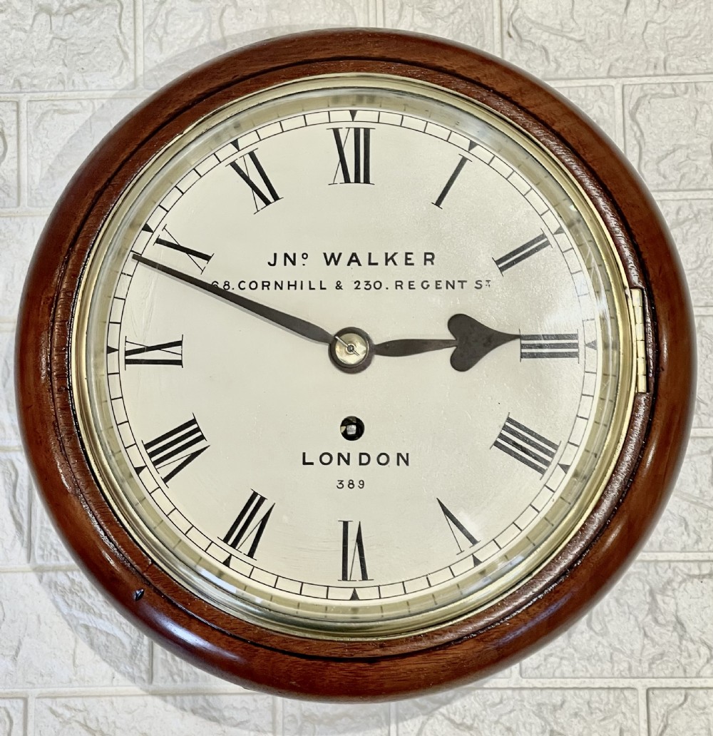 A circular antique mahogany wall clock featuring a cream dial with Roman numerals, spade hands, and a brass bezel.