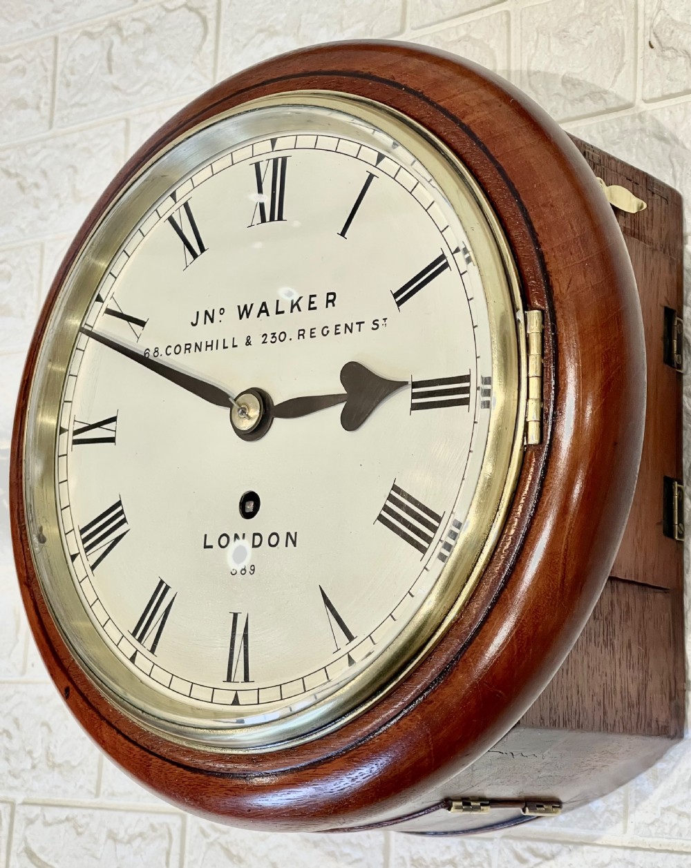 A circular antique mahogany wall clock featuring a cream dial with Roman numerals, spade hands, and a brass bezel. View II