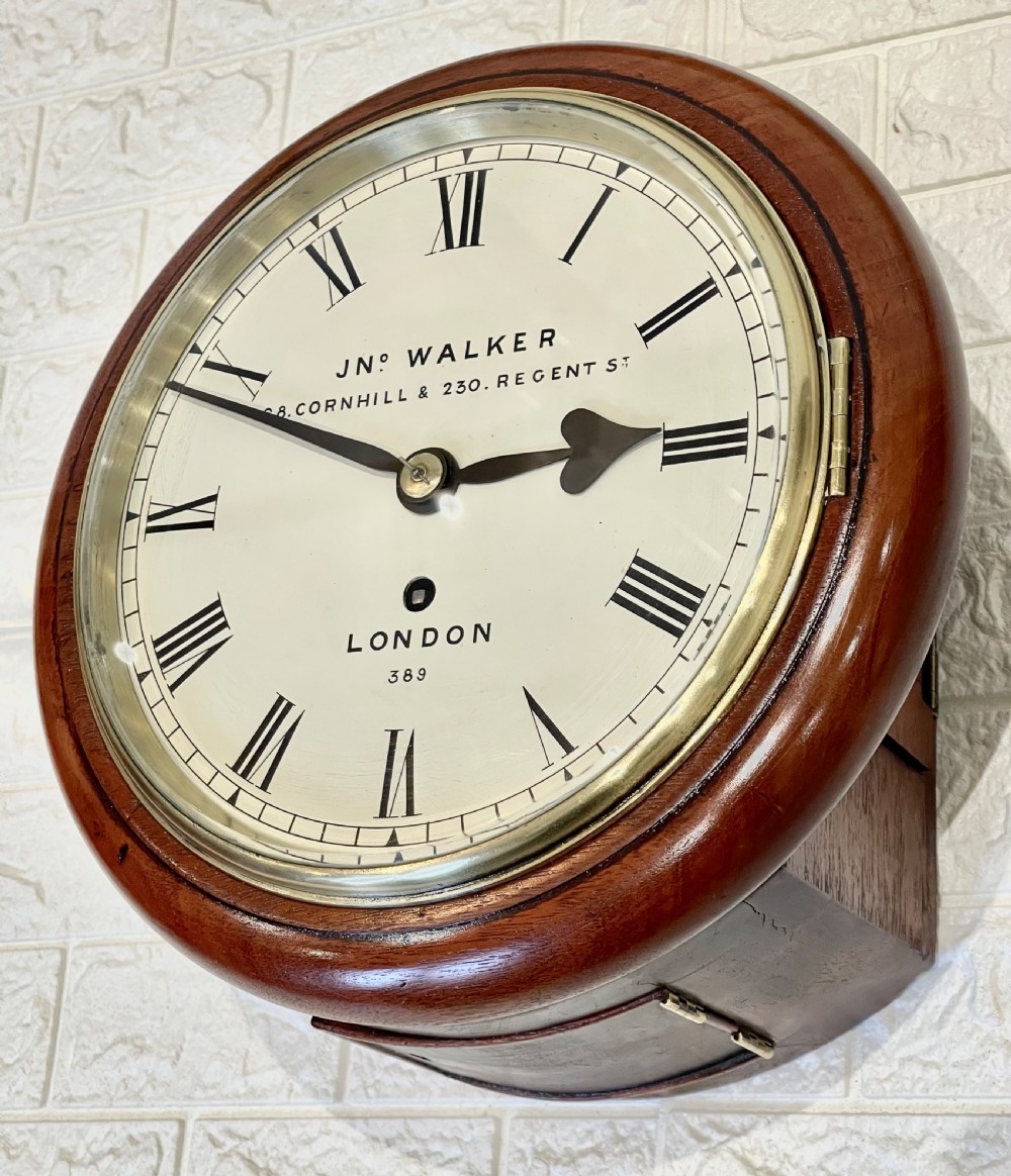 A circular antique mahogany wall clock featuring a cream dial with Roman numerals, spade hands, and a brass bezel. View III