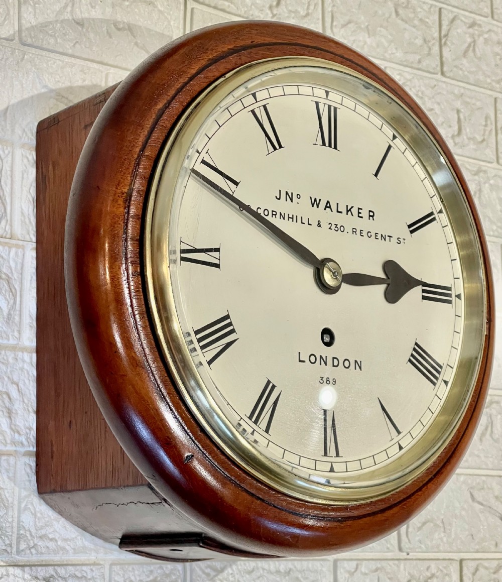 A circular antique mahogany wall clock featuring a cream dial with Roman numerals, spade hands, and a brass bezel. View IV