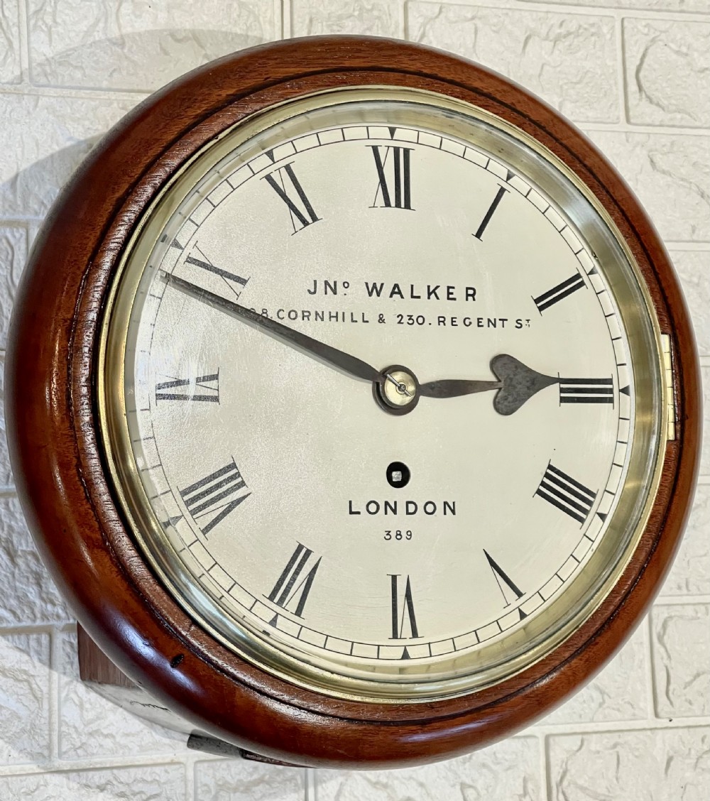 A circular antique mahogany wall clock featuring a cream dial with Roman numerals, spade hands, and a brass bezel. View VI