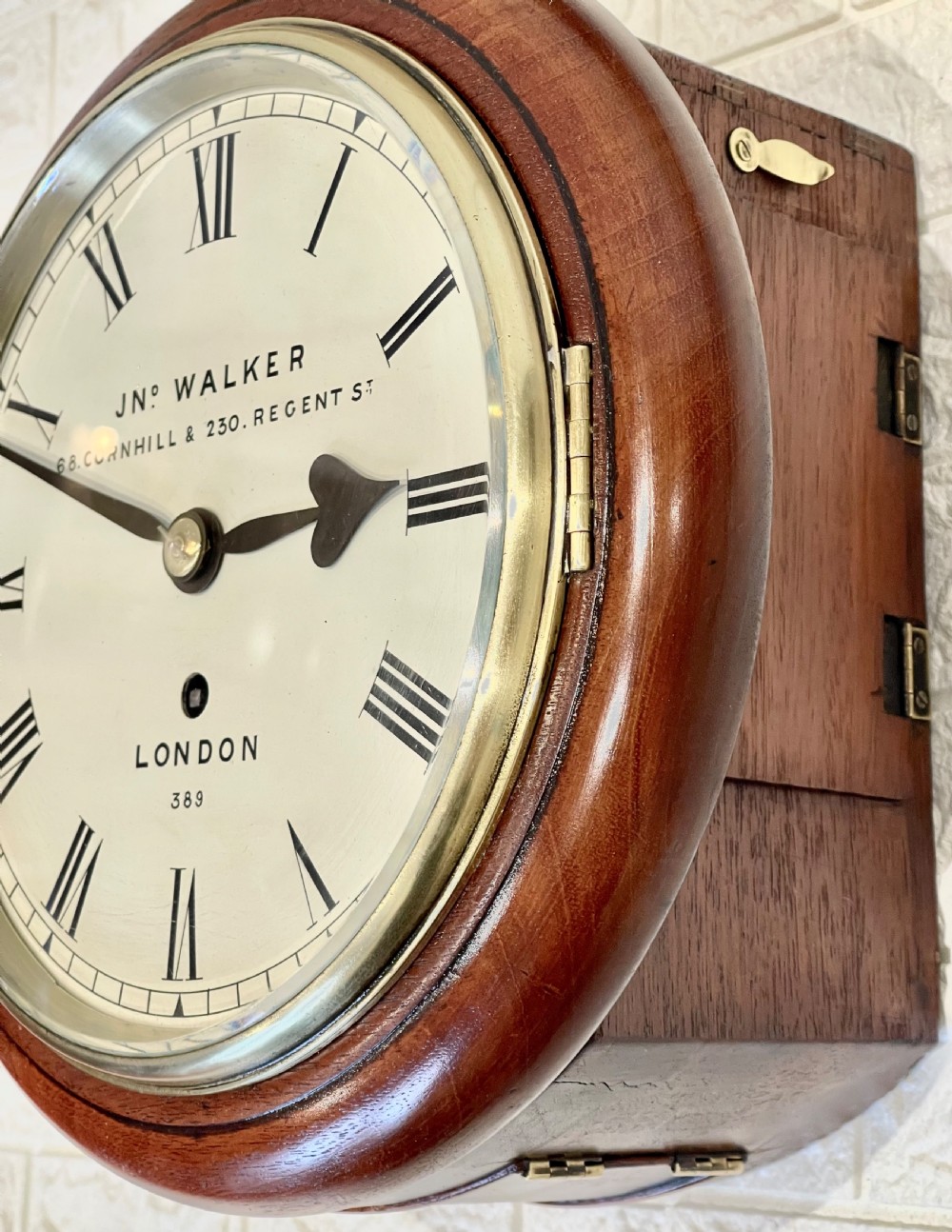 A circular antique mahogany wall clock featuring a cream dial with Roman numerals, spade hands, and a brass bezel. View IX