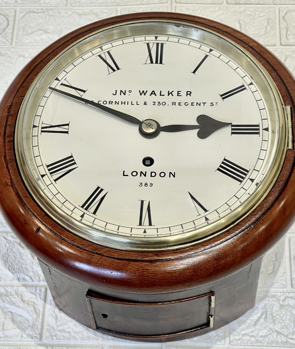 A circular antique mahogany wall clock featuring a cream dial with Roman numerals, spade hands, and a brass bezel. View XI