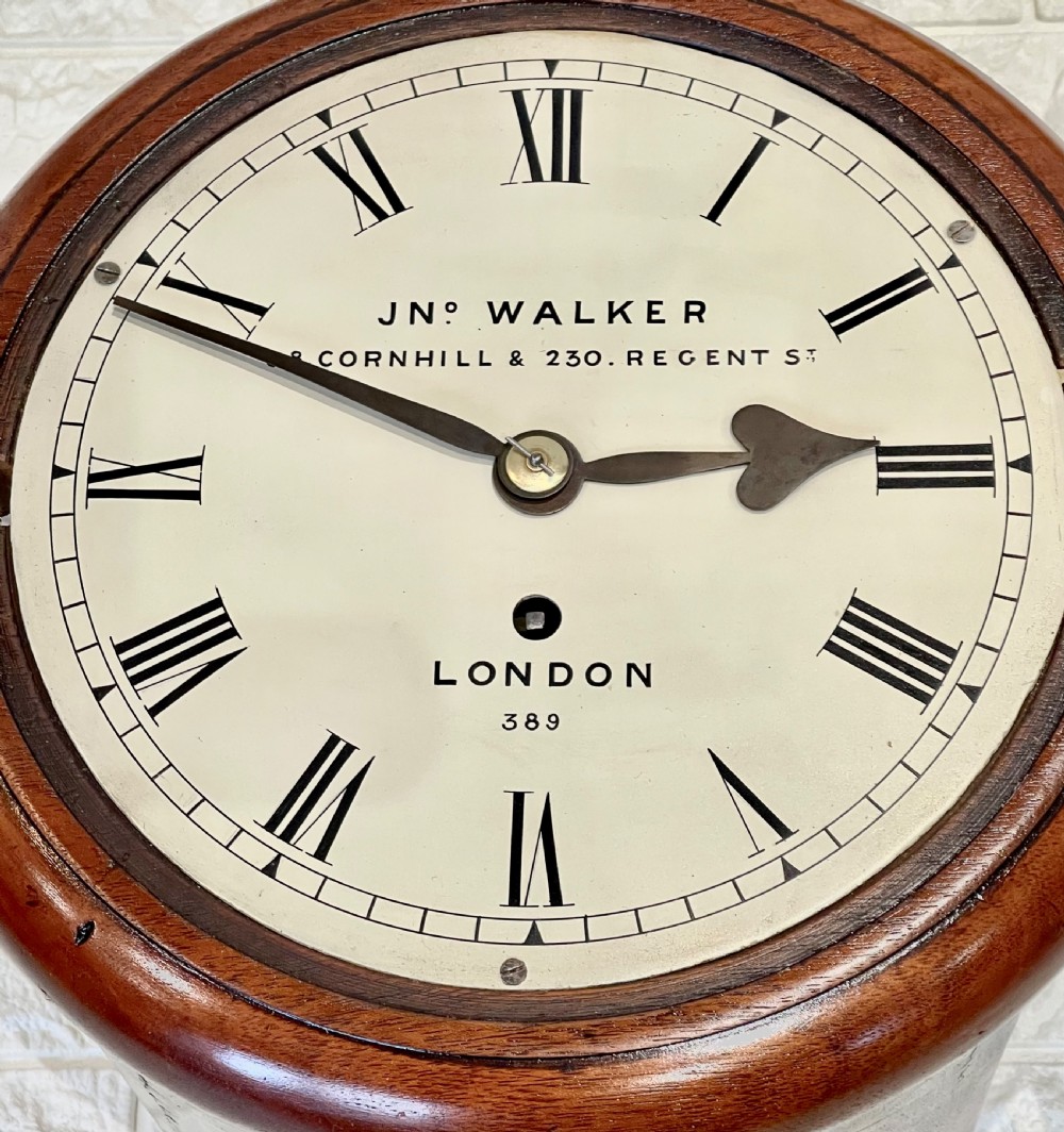 A circular antique mahogany wall clock featuring a cream dial with Roman numerals, spade hands, and a brass bezel. View XII
