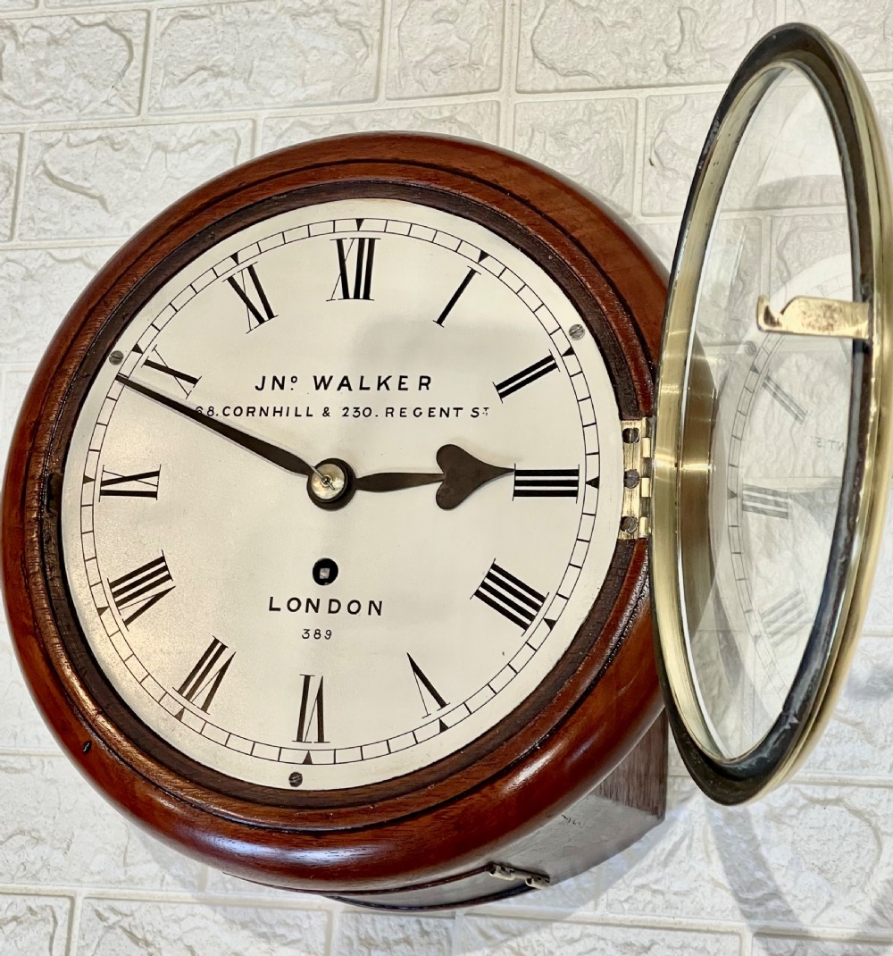 A circular antique mahogany wall clock featuring a cream dial with Roman numerals, spade hands, and a brass bezel. View XV