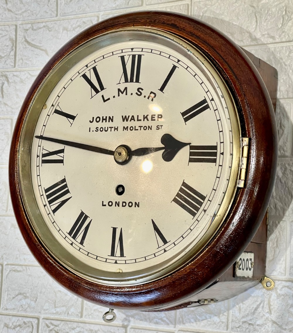 An antique circular mahogany wall clock with a brass-hinged glass bezel, white dial featuring Roman numerals, and black markings reading LMSR John Walker London.