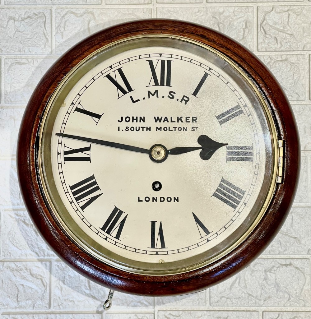An antique circular mahogany wall clock with a brass-hinged glass bezel, white dial featuring Roman numerals, and black markings reading LMSR John Walker London. View IV