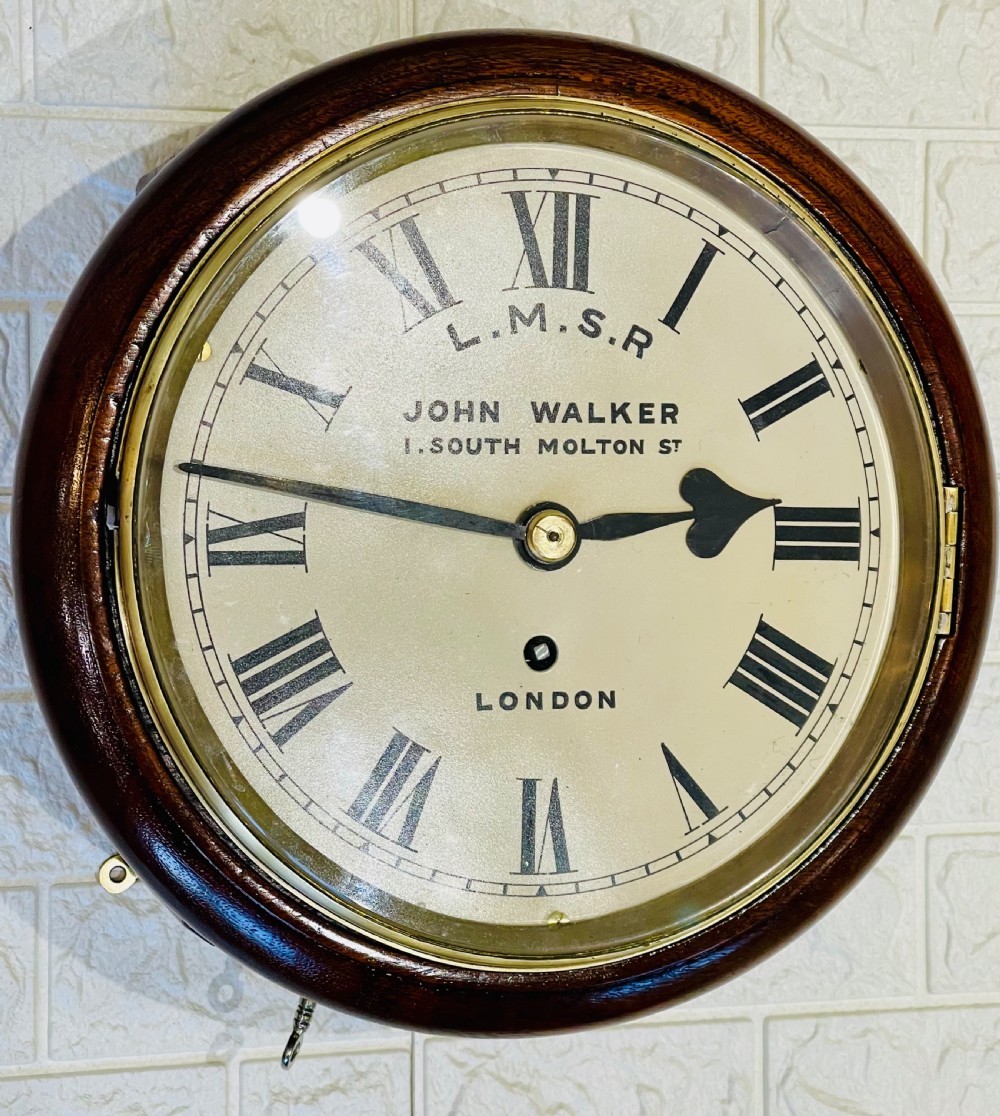 An antique circular mahogany wall clock with a brass-hinged glass bezel, white dial featuring Roman numerals, and black markings reading LMSR John Walker London. View VIII