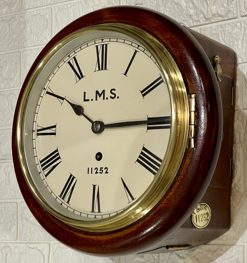 A circular mahogany wall clock with a brass bezel, off-white dial displaying Roman numerals, and London Midland and Scottish Railway branding.