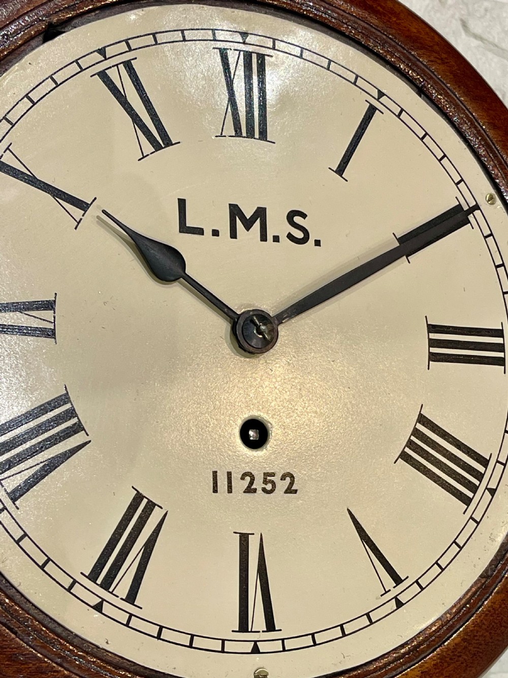 A circular mahogany wall clock with a brass bezel, off-white dial displaying Roman numerals, and London Midland and Scottish Railway branding. View III