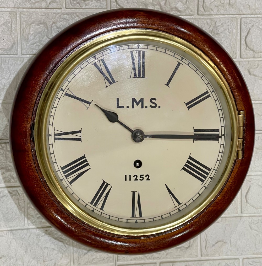 A circular mahogany wall clock with a brass bezel, off-white dial displaying Roman numerals, and London Midland and Scottish Railway branding. View IV