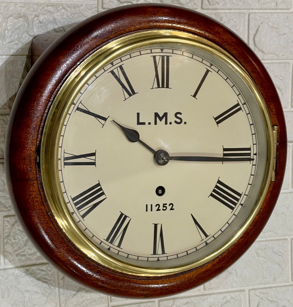 A circular mahogany wall clock with a brass bezel, off-white dial displaying Roman numerals, and London Midland and Scottish Railway branding. View V