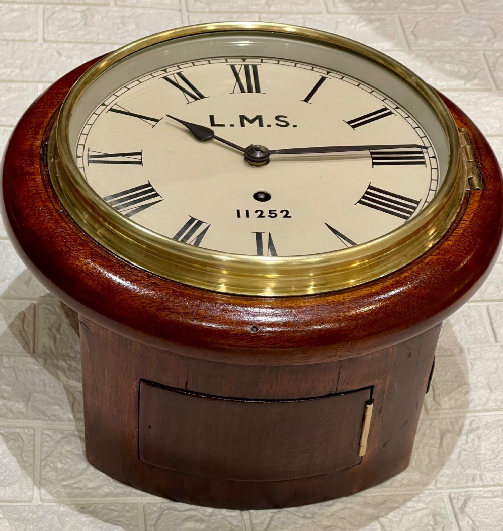 A circular mahogany wall clock with a brass bezel, off-white dial displaying Roman numerals, and London Midland and Scottish Railway branding. View VI