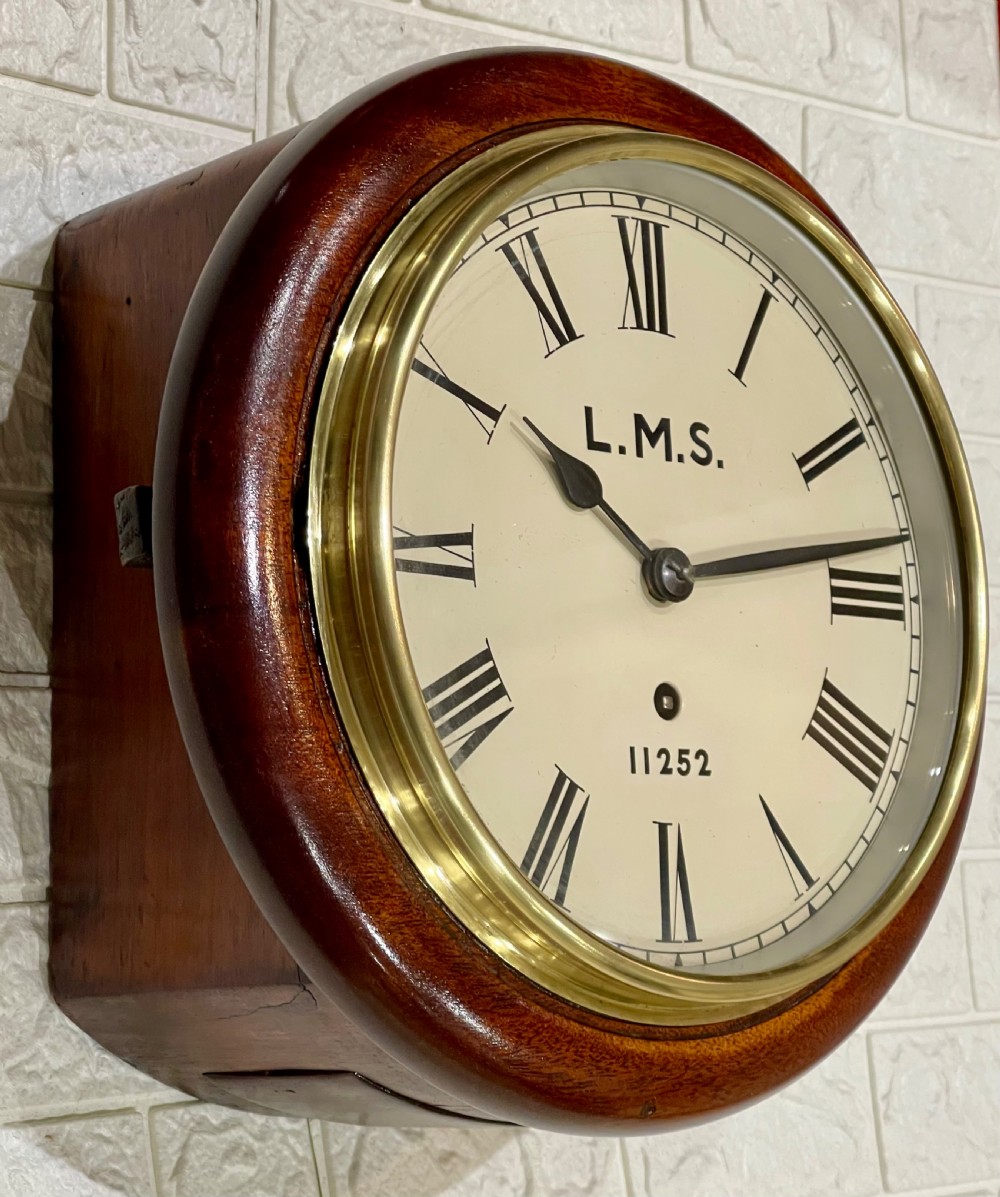A circular mahogany wall clock with a brass bezel, off-white dial displaying Roman numerals, and London Midland and Scottish Railway branding. View VII