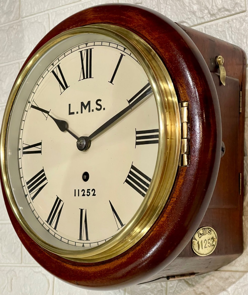 A circular mahogany wall clock with a brass bezel, off-white dial displaying Roman numerals, and London Midland and Scottish Railway branding. View IX