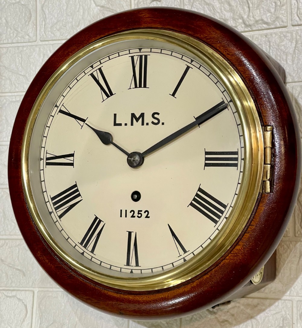 A circular mahogany wall clock with a brass bezel, off-white dial displaying Roman numerals, and London Midland and Scottish Railway branding. View X