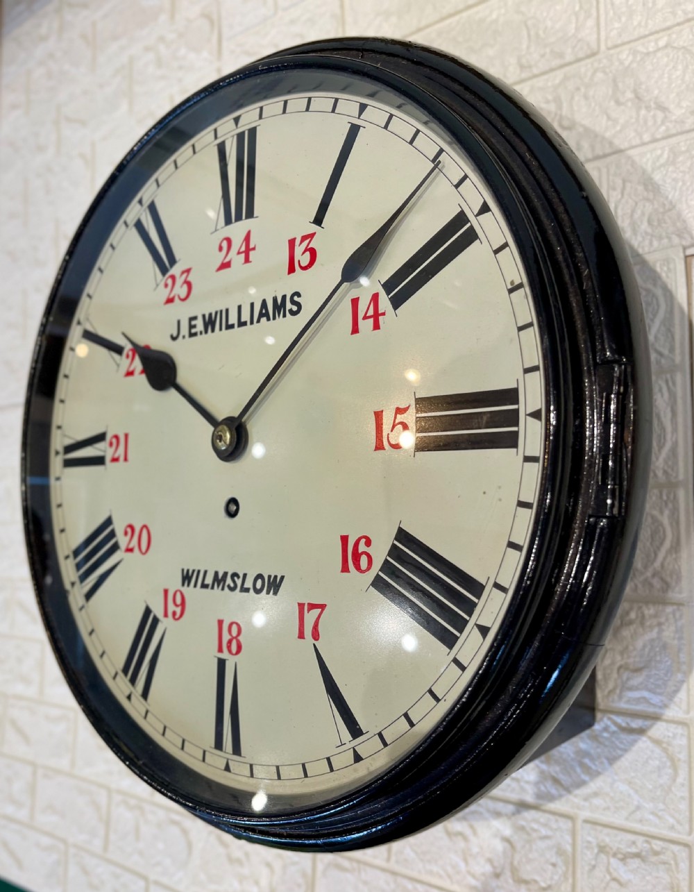 A circular Victorian wall clock featuring a black moulded surround, a cream dial with black Roman numerals, and red 24-hour markers signed J.E. Williams Wilmslow. View III