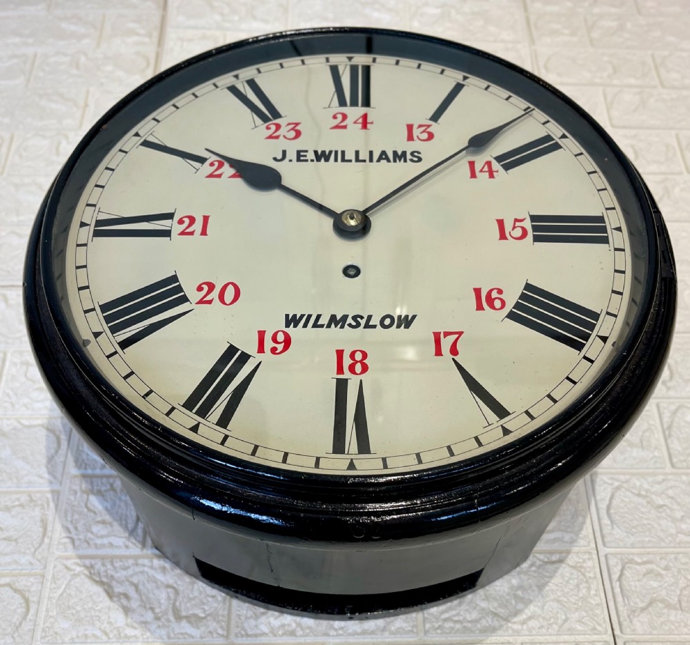 A circular Victorian wall clock featuring a black moulded surround, a cream dial with black Roman numerals, and red 24-hour markers signed J.E. Williams Wilmslow. View IV