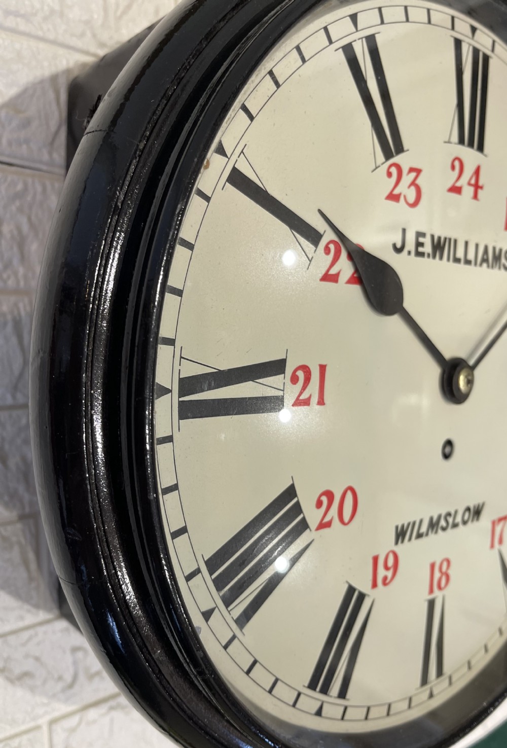 A circular Victorian wall clock featuring a black moulded surround, a cream dial with black Roman numerals, and red 24-hour markers signed J.E. Williams Wilmslow. View VI