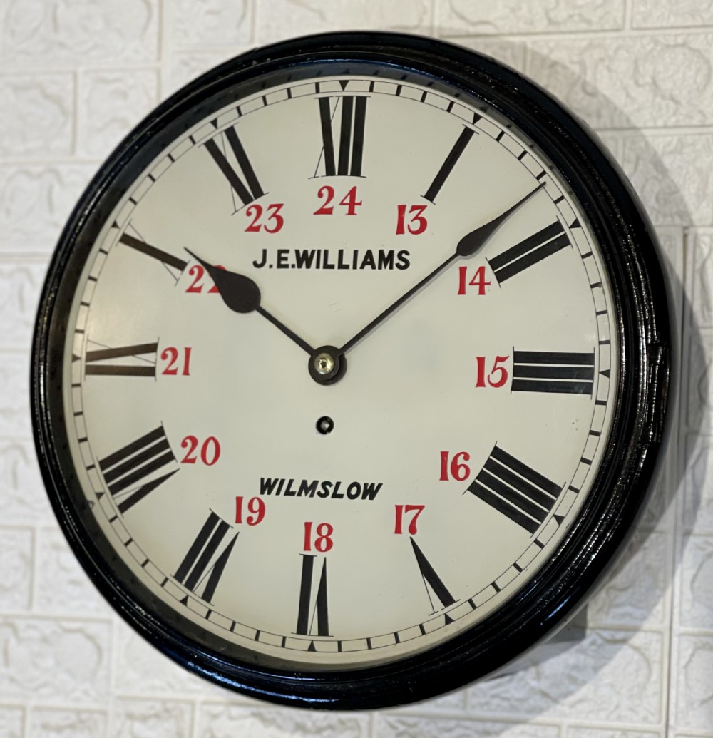 A circular Victorian wall clock featuring a black moulded surround, a cream dial with black Roman numerals, and red 24-hour markers signed J.E. Williams Wilmslow. View VII