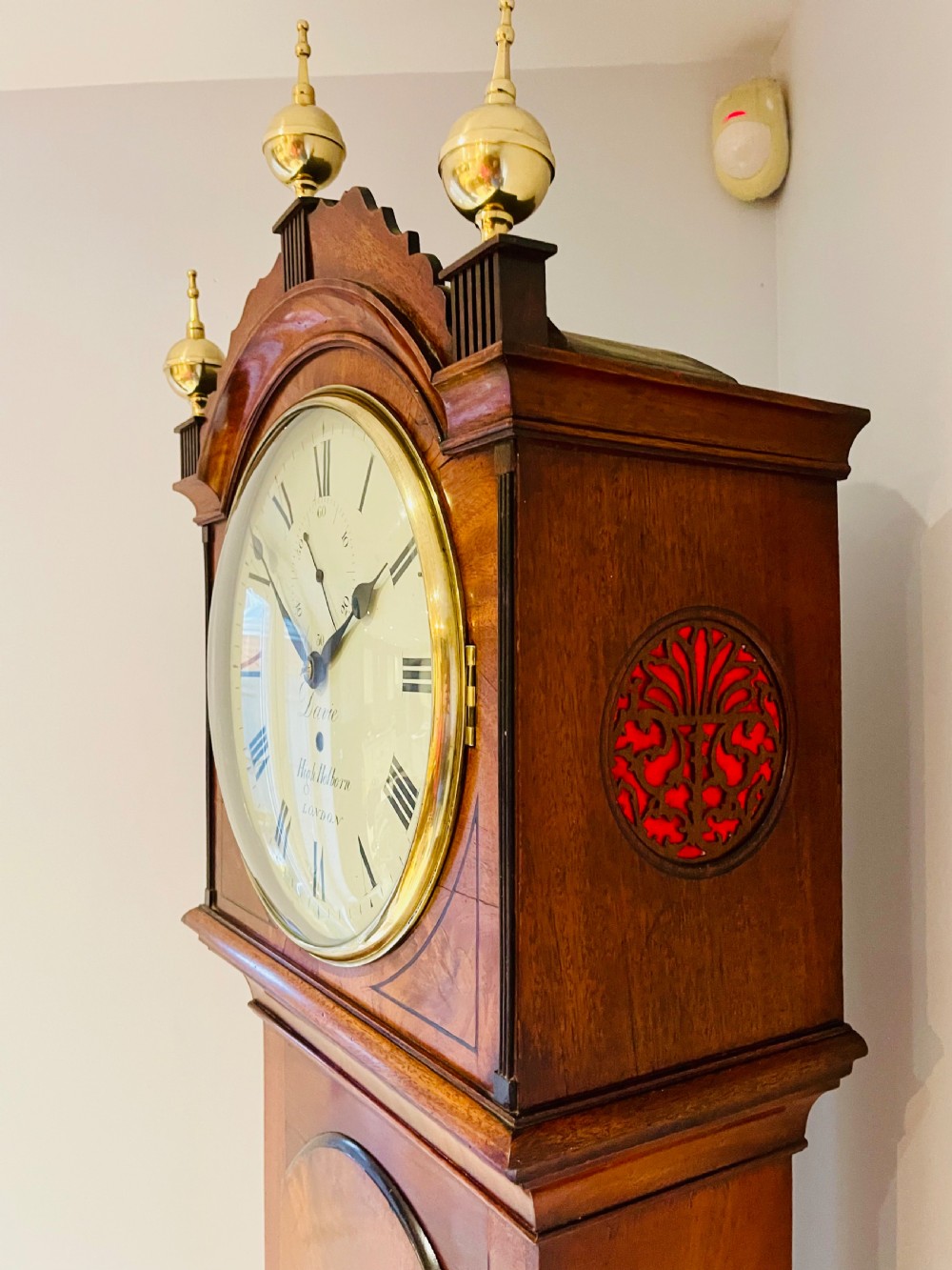 A Georgian flame mahogany longcase clock featuring three brass urn finials, a circular dial signed Davie High Holborn London, and a long arched trunk door. View IX