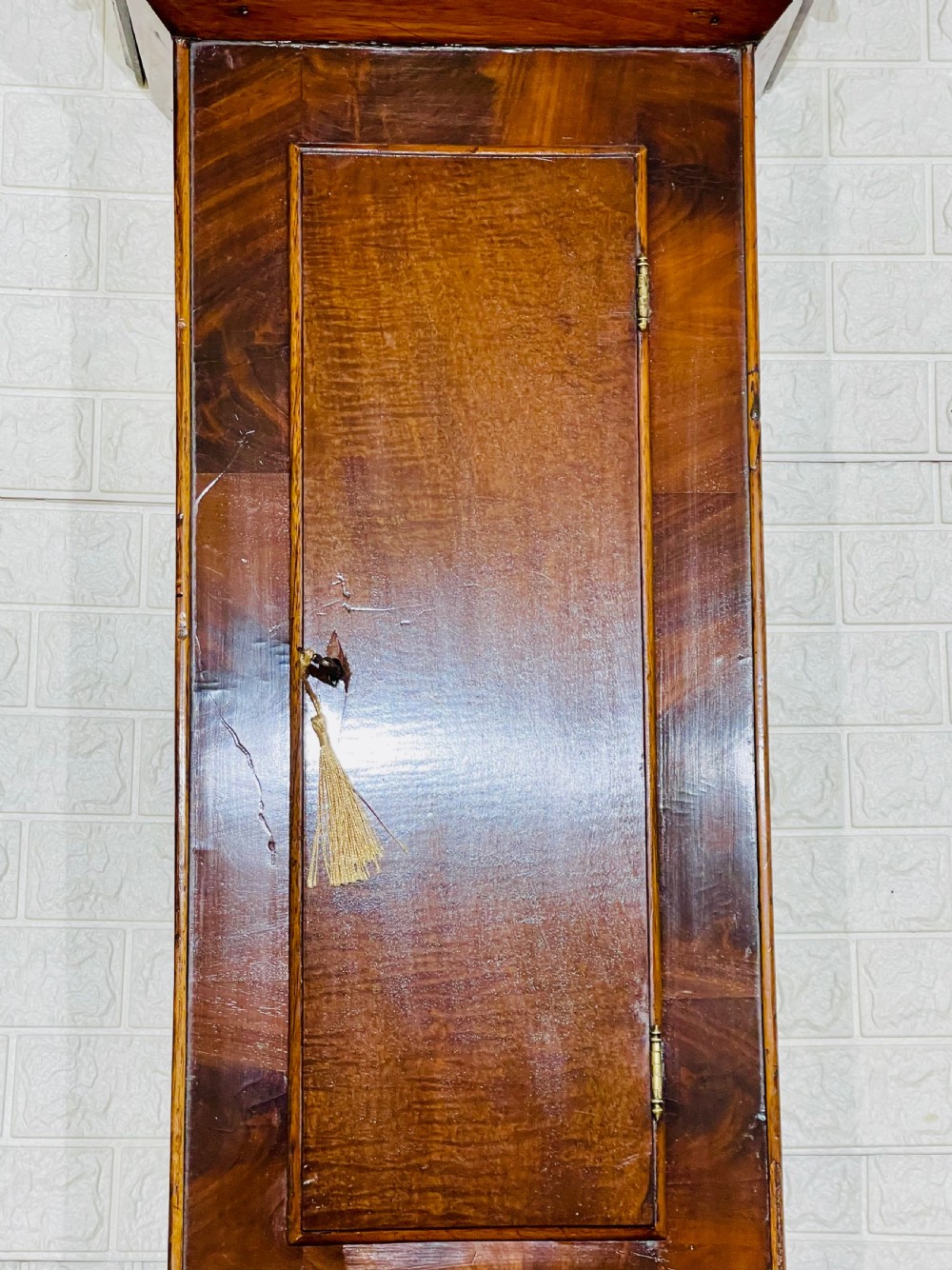 An antique Regency mahogany wall clock featuring an octagonal dial frame, carved floral shoulders, and a long trunk door with a key tassel. View VIII