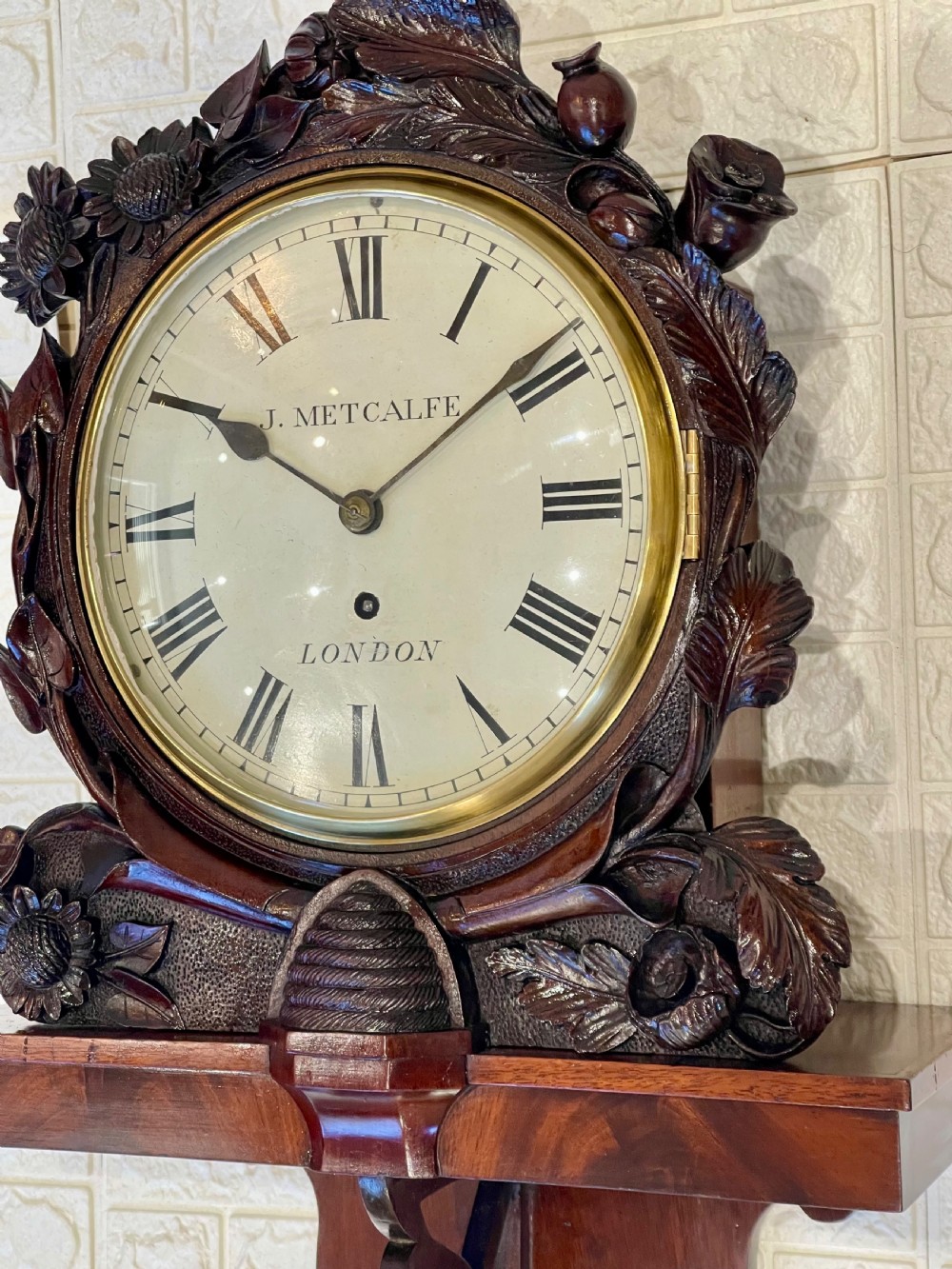A Victorian carved mahogany fusee wall clock with Roman numerals on a white dial framed by carved floral details, resting on a matching wooden wall bracket. View II
