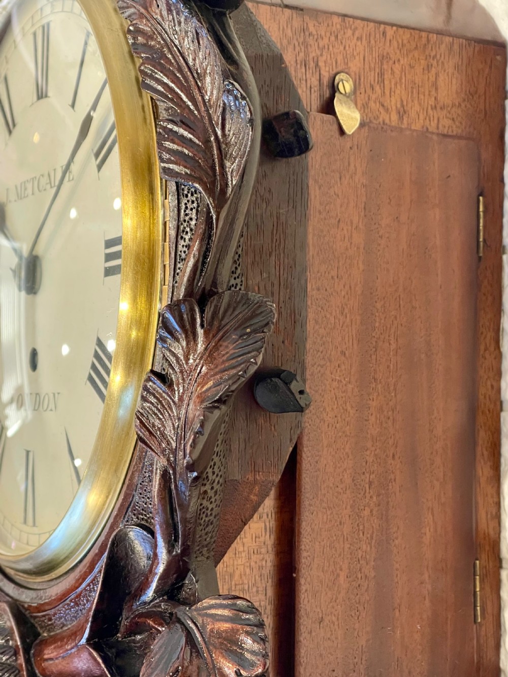 A Victorian carved mahogany fusee wall clock with Roman numerals on a white dial framed by carved floral details, resting on a matching wooden wall bracket. View VI