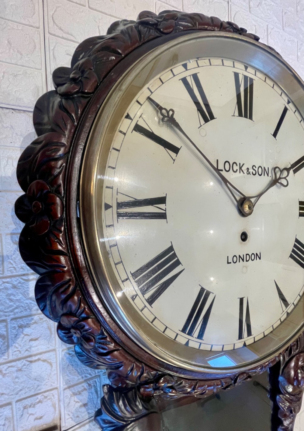 An antique dark mahogany drop dial wall clock featuring a white dial face with Roman numerals and a visible brass pendulum. View IX