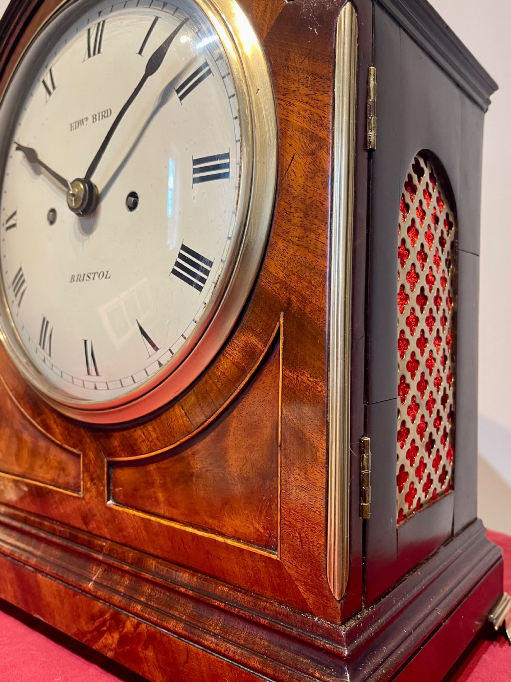 A George III mahogany bracket clock featuring an arched top with a brass handle, a circular white dial with Roman numerals, and brass bracket feet. View II