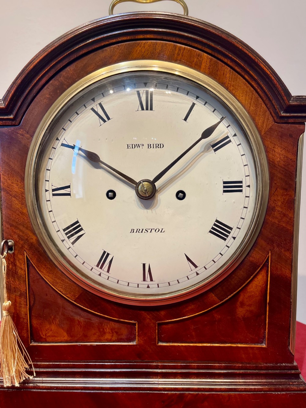 A George III mahogany bracket clock featuring an arched top with a brass handle, a circular white dial with Roman numerals, and brass bracket feet. View III