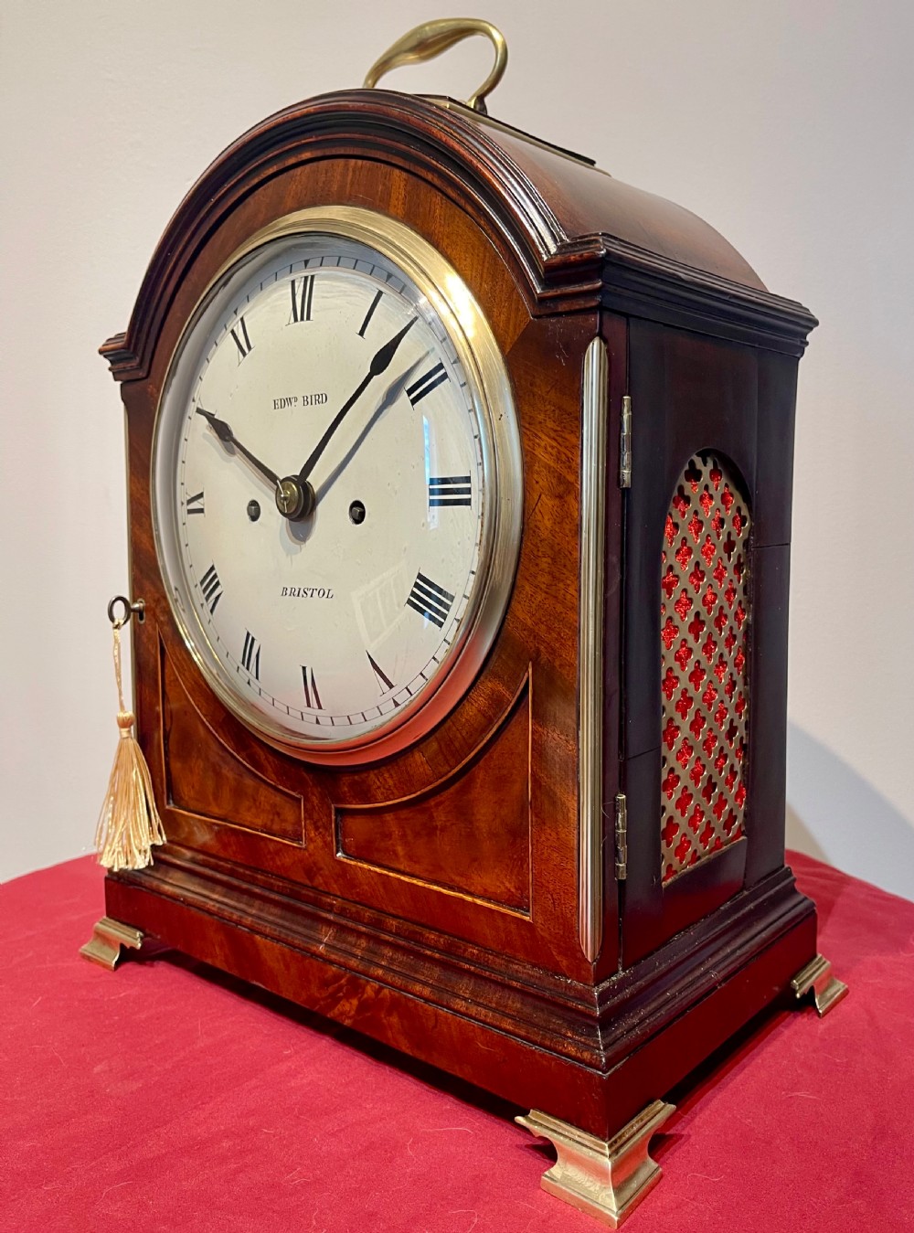 A George III mahogany bracket clock featuring an arched top with a brass handle, a circular white dial with Roman numerals, and brass bracket feet. View VII