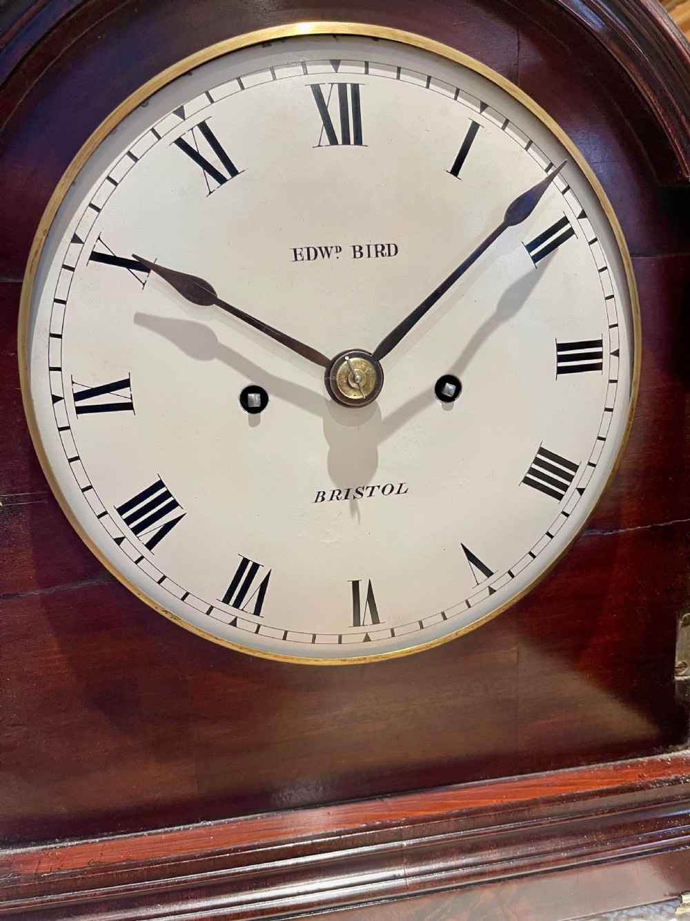 A George III mahogany bracket clock featuring an arched top with a brass handle, a circular white dial with Roman numerals, and brass bracket feet. View XIV